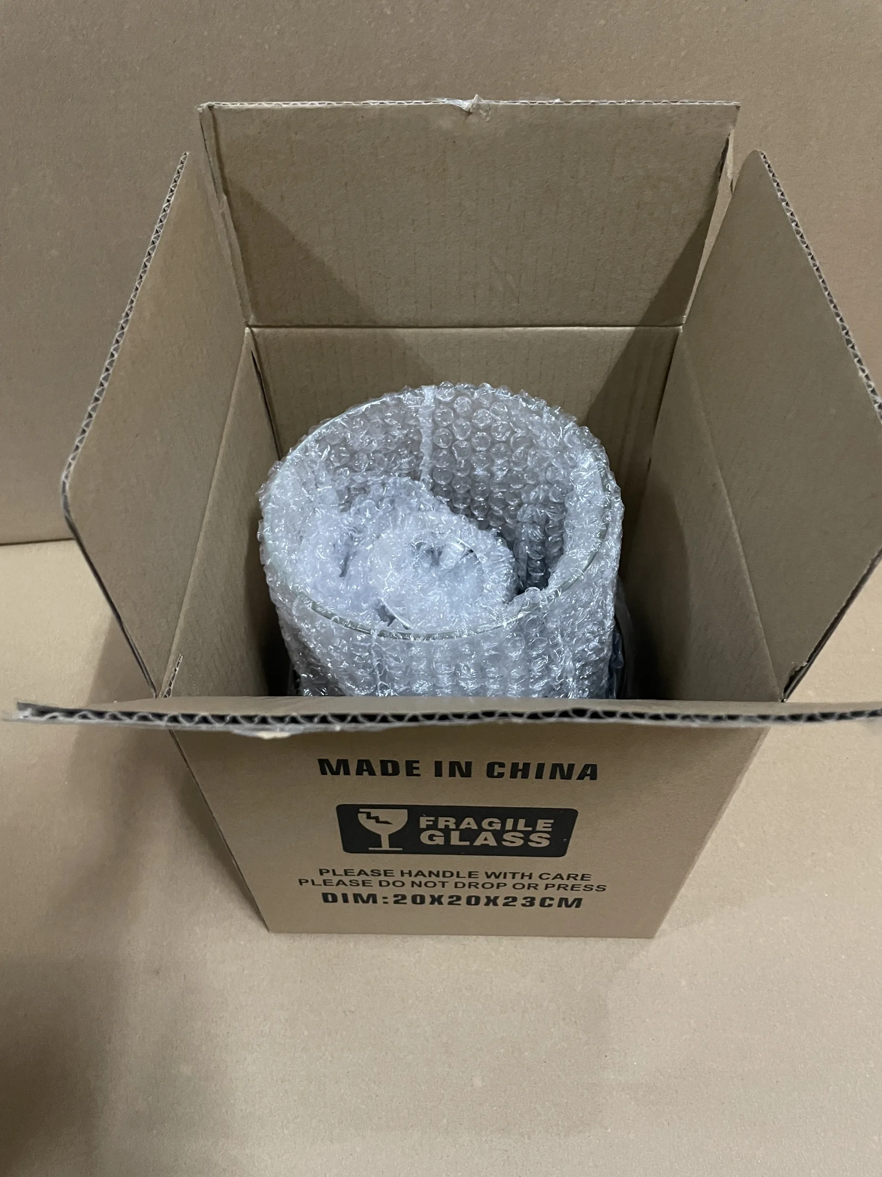 Open carton containing a cylindrical tabletop fireplace wrapped in bubble packaging